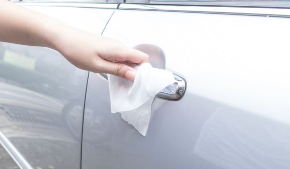 Woman hand cleaning removing germs with antibacterial wet wipes on car door handle for corona virus COVID-19 coronavirus prevention.