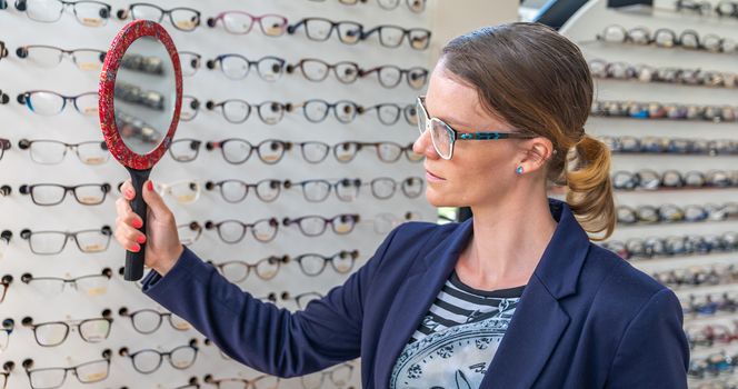 business woman tries glasses in front of a mirror in an optics store.