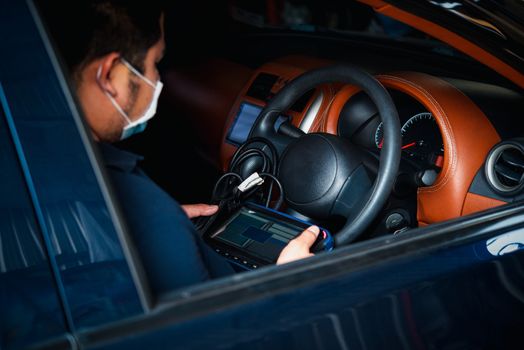 Car mechanic or serviceman checking a car engine by OBD-II electric tools for fix and repair problem at car garage or repair shop