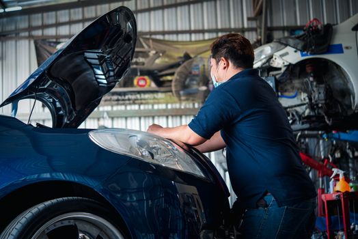 Car mechanic or serviceman checking a car engine for fix and repair problem at car garage or repair shop