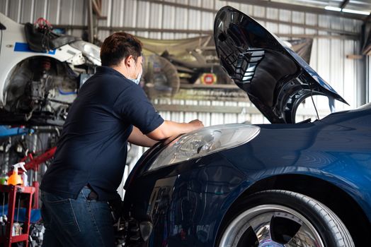 Car mechanic or serviceman checking a car engine for fix and repair problem at car garage or repair shop