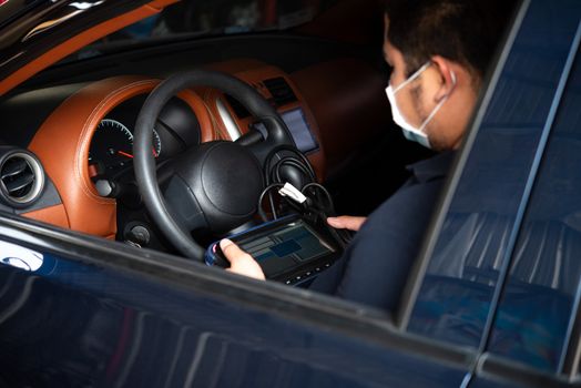 Car mechanic or serviceman checking a car engine by OBD-II electric tools for fix and repair problem at car garage or repair shop