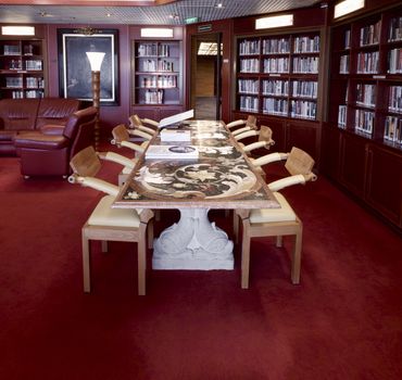 Classical Library Room With Leather Armchairs, Stone Table And World Atlas On The Table