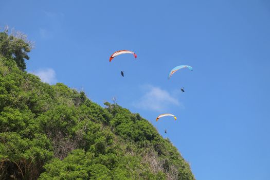 Paragliding in the sky. Three single paragliders flying in summer day over tropical Bali island. Beautiful paraglider in flight on a turquise background. Concept of active lifestyle and extreme sport.