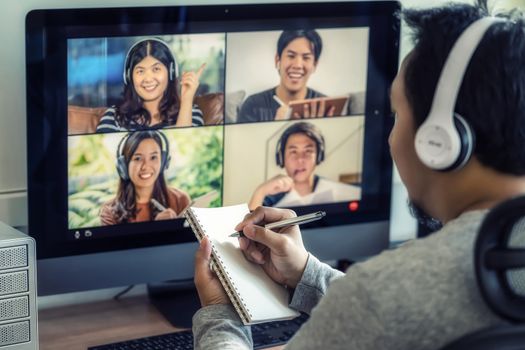 Closeup Asian man hand writing notebook when online learning via video conference with colleague and team building meeting when Covid-19 pandemic,Coronavirus outbreak,online meeting,new normal concept