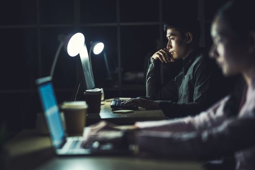 Asian businesswoman and businessman working hard late together with technology computer in office, customer service and call center, team work with colleagues for success achievement project concept