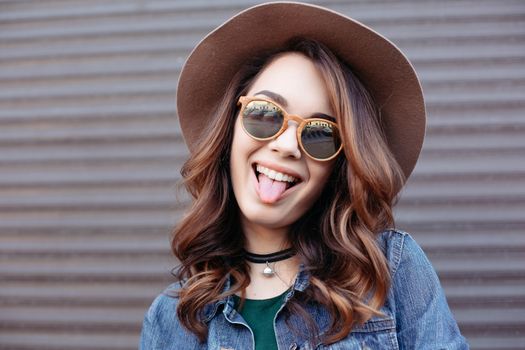 Fashionable brunette in brown hat, jeans jacket and choker on neck posing at street,looking at camera. Confident stylish woman with handbag, after beauty salon and shopping. Street swag style.