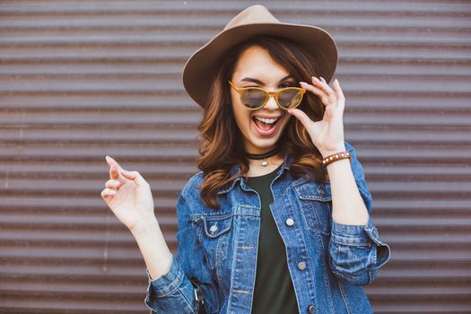 Happy beautiful brunette woman in sunglasses, striped white and black blouse smiling at camera, posing at camera. Gorgeous girl with perfect skin, plump lips, wavy hair. Walking at street. Sunset.