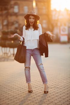 Beautiful positivity brunette woman in hat, white blouse, jeans walking at sunset in city, after shopping and beauty salon. Smiling fashionable girl stylish wearing posing at camera. Hipster look.