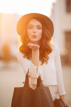 Beautiful positivity brunette woman in hat, white blouse, jeans walking at sunset in city, after shopping and beauty salon. Smiling fashionable girl stylish wearing posing at camera. Hipster look.