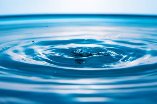 Water drops on blue surface. Water ripple background. Splashes from a drop of water. Raindrops on a blue background. The texture of the water. Aqua, turquoise, macro
