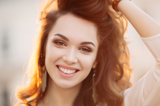 Portrait of young and beautiful brunette woman emotionally smiling, walking at street,posing, looking away. Girl in hat, with big earrings with perfect make up and wavy hairstyle. Street fashion look.