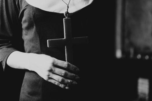 People and religion, catholic sister praying in church and holding cross in hands. Black and white