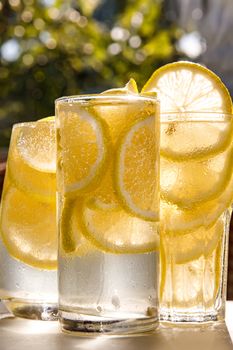 Three glasses of lemon water on the sunny garden background. Close-up view