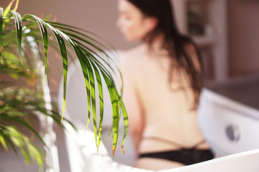 Pretty girl in bathroom - white bath. Green plant and blurred background