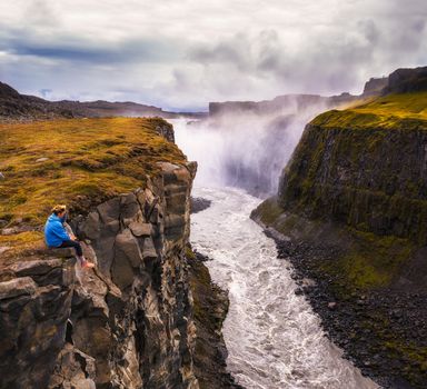 Aerial view of a young hiker sitting at the edge of the Gullfoss waterfall, also known as the Golden Falls, located on the Olfusa river in southwest Iceland