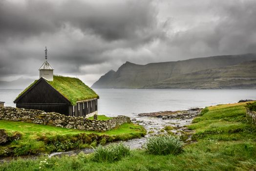 Small village church in Funningur under heavy clouds. Funningur is located on the island of Eysturoy, Faroe Islands, Denmark