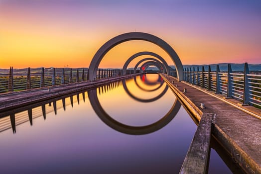 Falkirk Wheel at sunset. Falkirk Wheel is a rotating boat lift in Scotland and connects the Forth and Clyde Canal with the Union Canal. Long exposure.