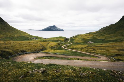 Winding road on Faroe Islands towards the village of Nordradalur surrounded by beatiful scenery and with Atlantic Ocean in the background