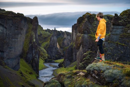 Young hiker standing at the edge of the Fjadrargljufur Canyon in Iceland. Fjadrargljufur Canyon is about 100 meters deep and about 2 kilometers long and it is located in South East of Iceland.