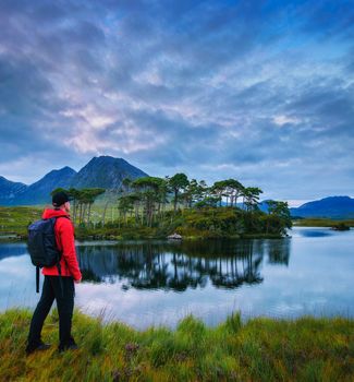 Young hiker with a backpack looking at the Pine Island in Derryclare Lough, Galway county, Ireland