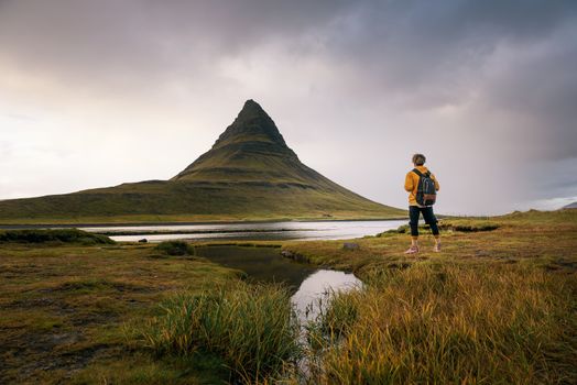 Young hiker with a backpack looks at the Kirkjufell mountain in Iceland. This 463 m high mountain is located on the north coast of Iceland's Snaefellsnes peninsula.