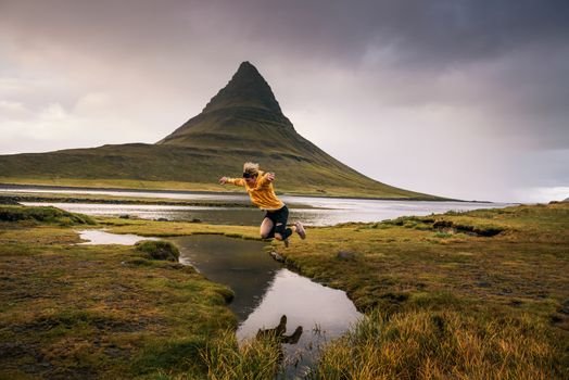 Young hiker jumps over a stream at the Kirkjufell mountain in Iceland. This 463 m high mountain is located on the north coast of Iceland's Snaefellsnes peninsula.