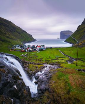 Waterfall and the village of Tjornuvik located on the coast of a beautiful bay in the Faroe Islands, Denmark. Long exposure.