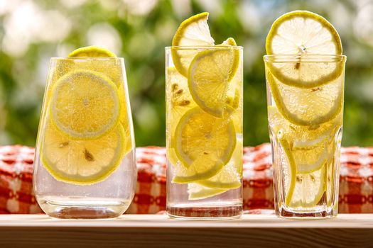 Three glasses of lemon water on the sunny garden background