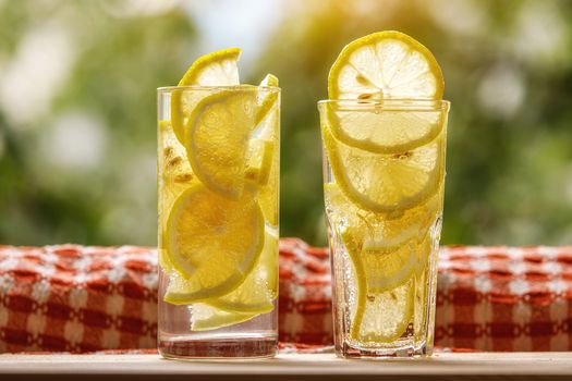 Glasses of lemonade with lemon on the sunny garden background