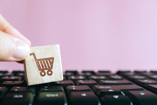 Closed up shopping cart icon on wood cube on computer keyboard. Online shoping business technology concept.