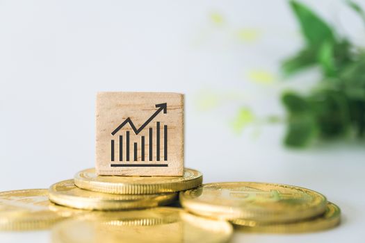 Graph rising up growht exponencial sign on wooden cube with objects such as gold coin, calculator and mini home model behide white clean background. Business financial loan property concept.