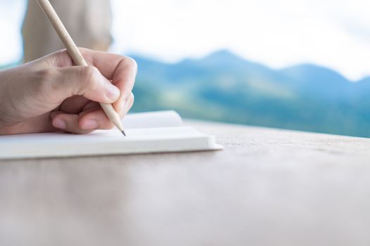 Woman hand writing down in small white memo notebook for take a note not to forget or to do list plan for future.