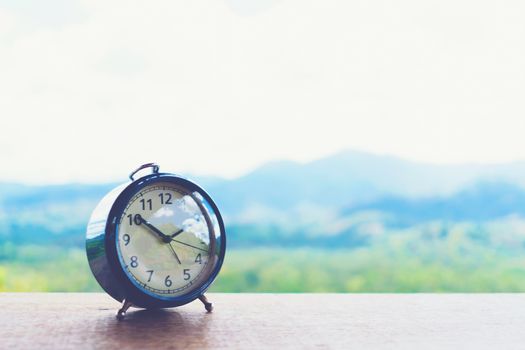 Selective focus of alarm clock on table with nature bokeh mountain background. Time in life concept
