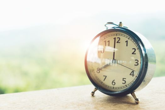 Selective focus of alarm clock on table with nature bokeh mountain background. Time in life concept