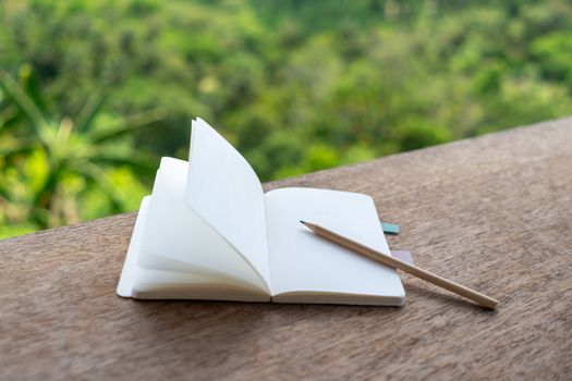 Small white notebook on table with mountain view background.