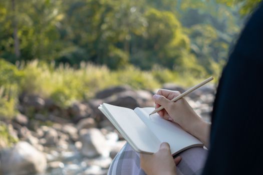 Woman hand writing down in small white memo notebook for take a note not to forget or to do list plan for future.