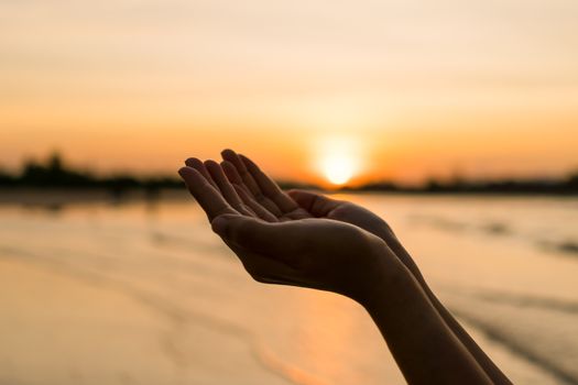 Woman hands place together like praying in front of nature blur beach sunset sky background.