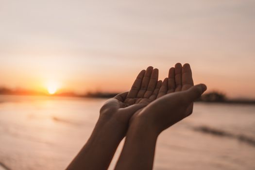 Woman hands place together like praying in front of nature blur beach sunset sky background.