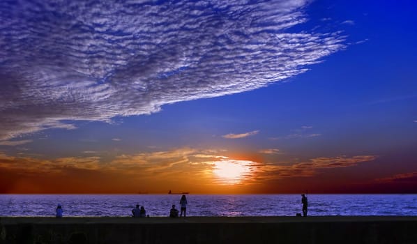 Beautiful dramatic ocean sunset and cloudscape with people watching from a pier