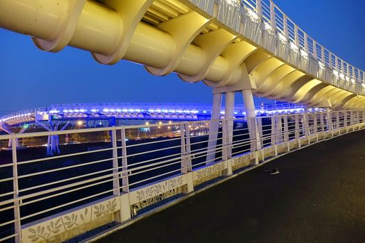 A modern overpass for bikes and pedestrians lit up at evening time

