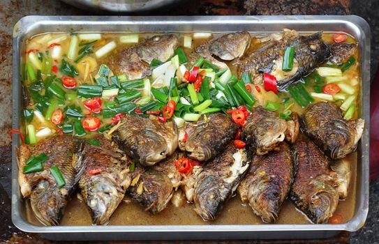 An outdoor food stall sells braised fish with chilies and scallion