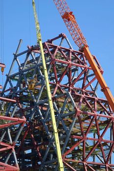 A major construction project with steel girders and cranes against a blue sky
