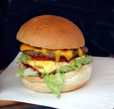 A delicious looking hamburger with lettuce, tomatoes, cheese and egg
