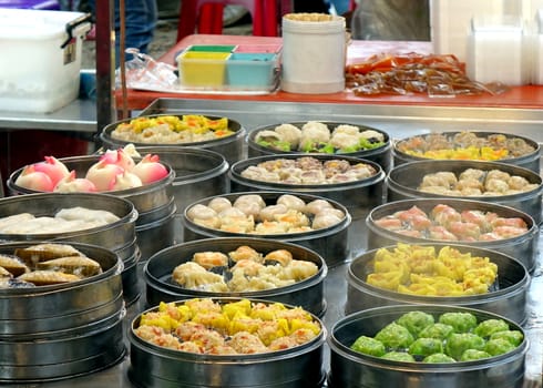 An outdoor vendor sells Cantonese Dim Sum dishes cooked in metal steamers