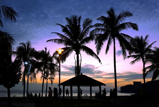 Tropical beach scene with palm trees at dusk with people as silhouettes
