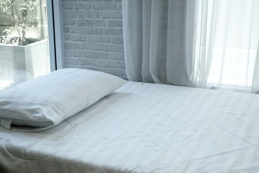 white pillow on mattress bed beside see through sheer window curtain