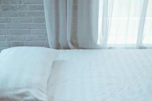 white pillow on mattress bed beside see through sheer window curtain