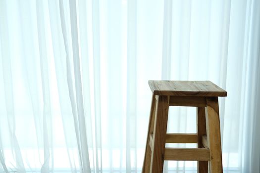 wooden bar stool chair beside see through sheer window curtain