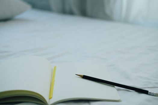 opening notebook & pencil on white bed mattress
